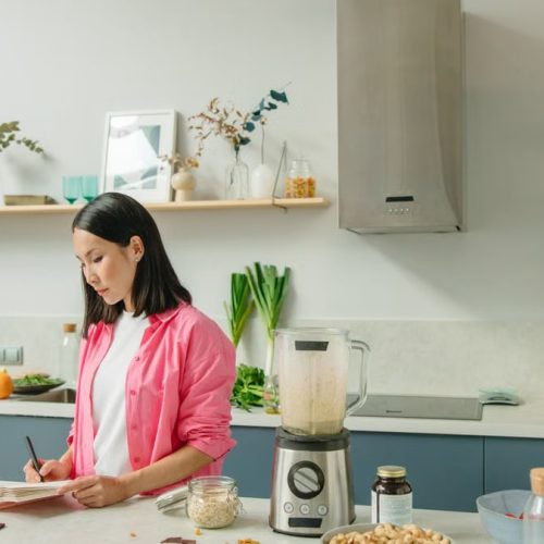 Asian woman writing in a notebook while cooking in a stylish kitchen.