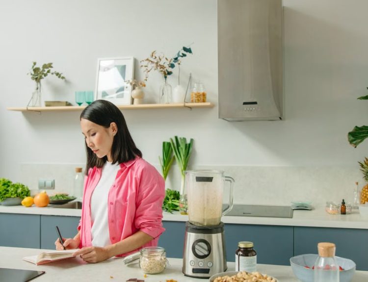 Asian woman writing in a notebook while cooking in a stylish kitchen.