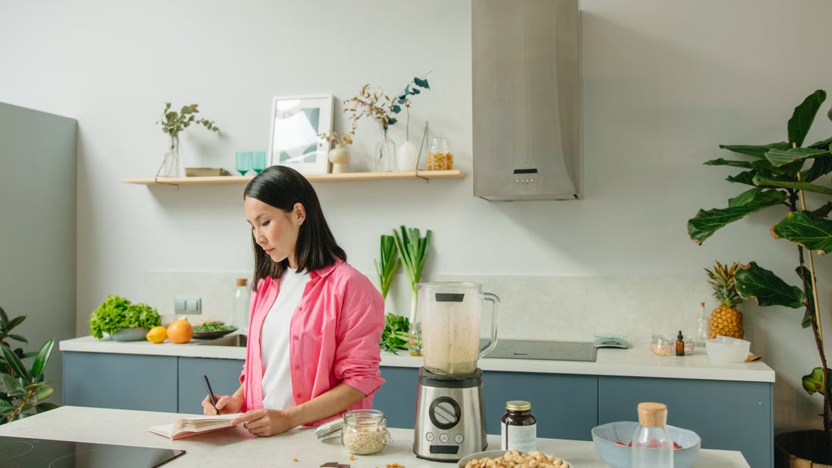 Asian woman writing in a notebook while cooking in a stylish kitchen.